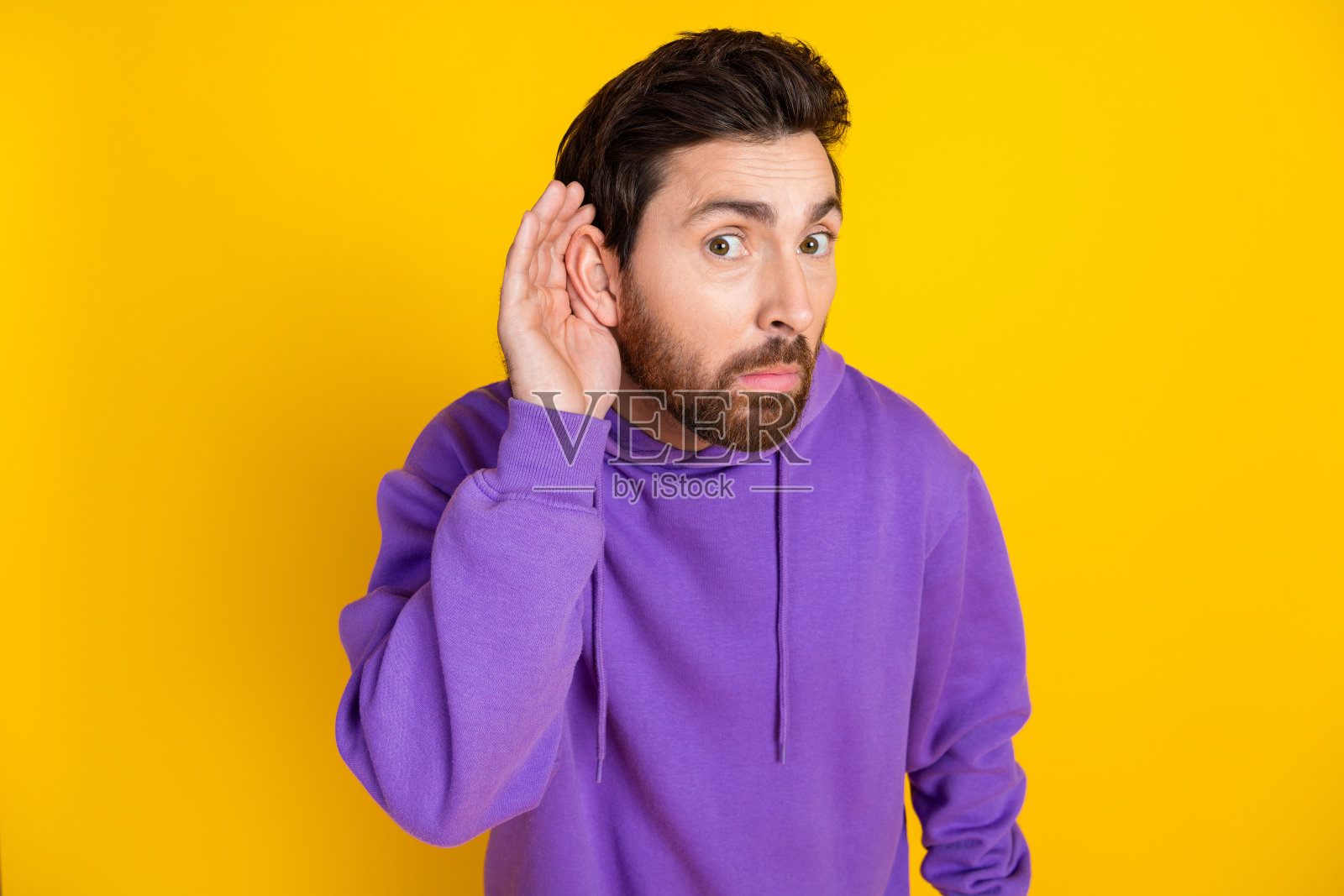 惊讶的男人的肖像,时尚的鬃毛穿着紫色卫衣,手放在耳朵上,听秘密隔离在黄色背景上照片摄影图片
