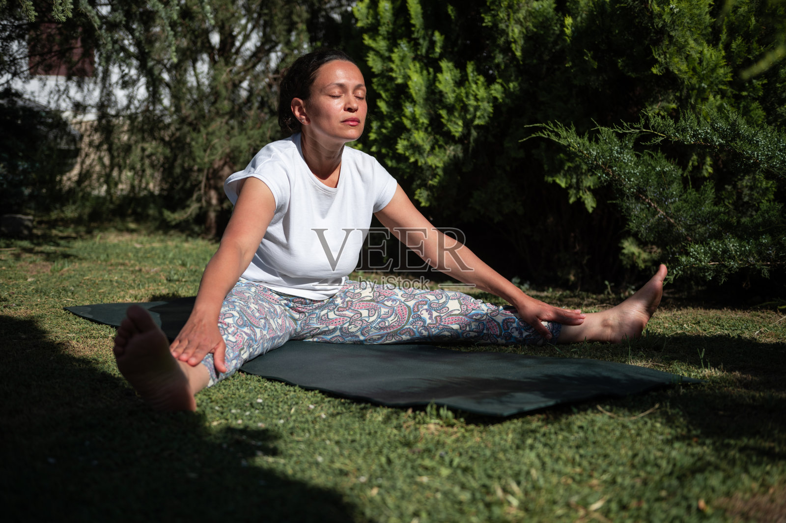 一名女子在花园里安详地练习瑜伽,做坐姿前屈照片摄影图片