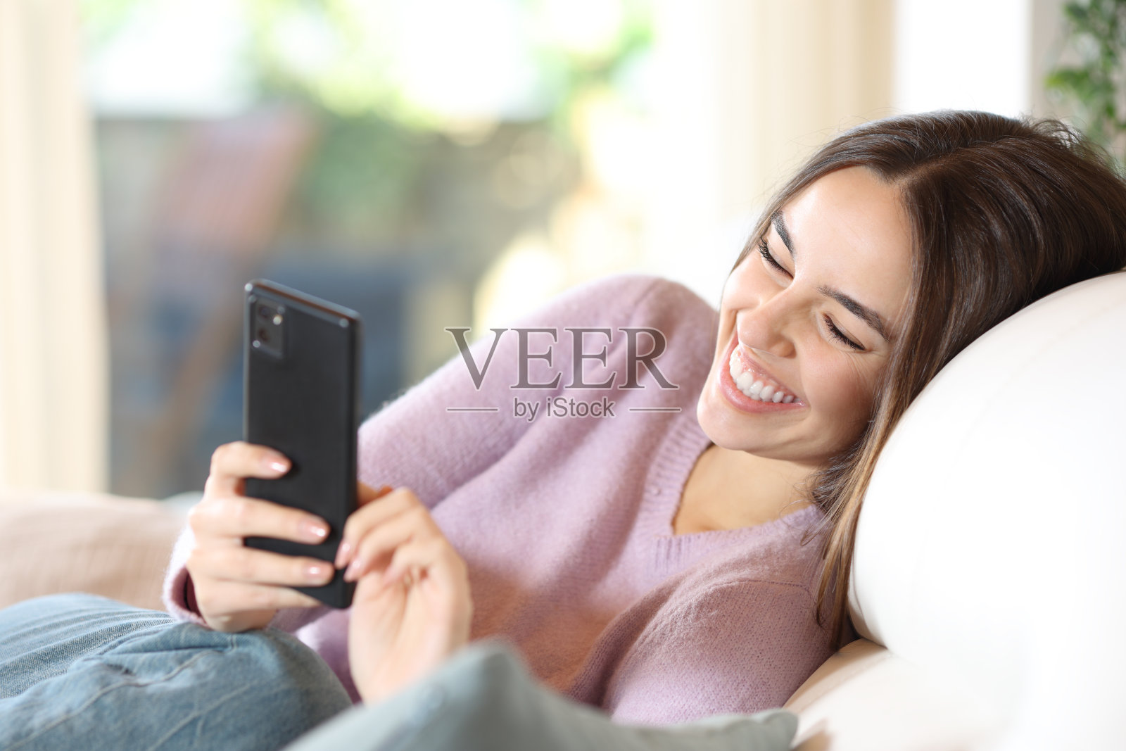 坐在沙发上看智能手机的快乐女人照片摄影图片