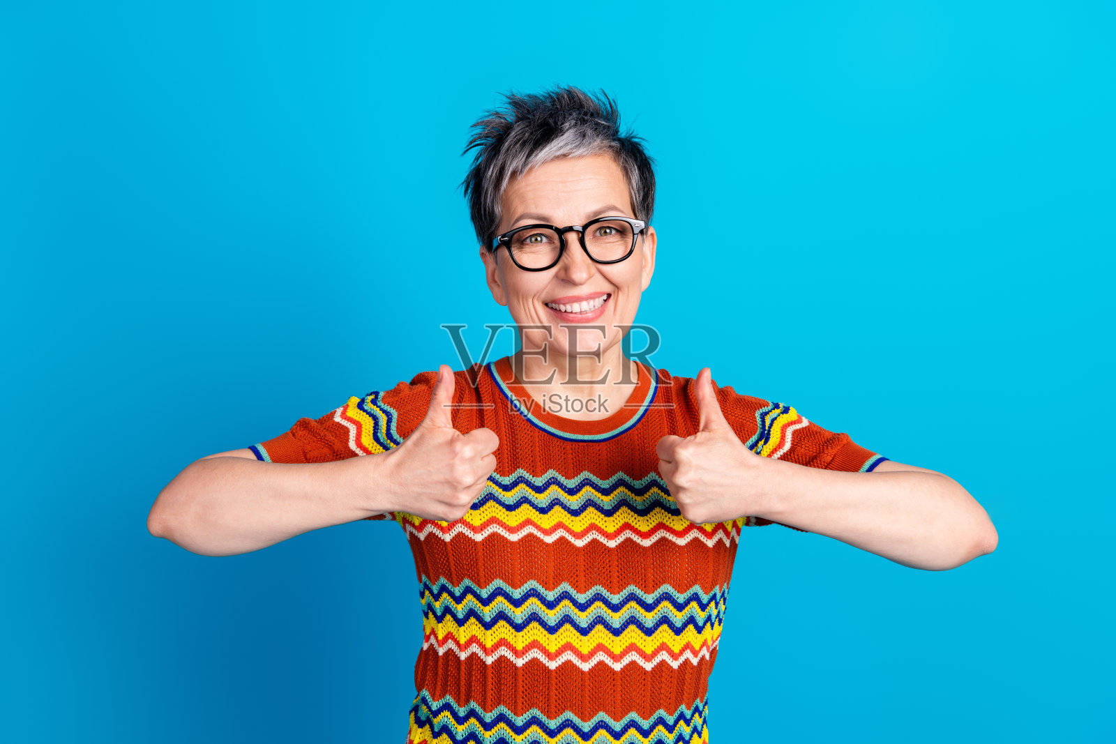 照片中漂亮的老妇人大拇指朝上,穿着蓝色背景的t恤照片摄影图片