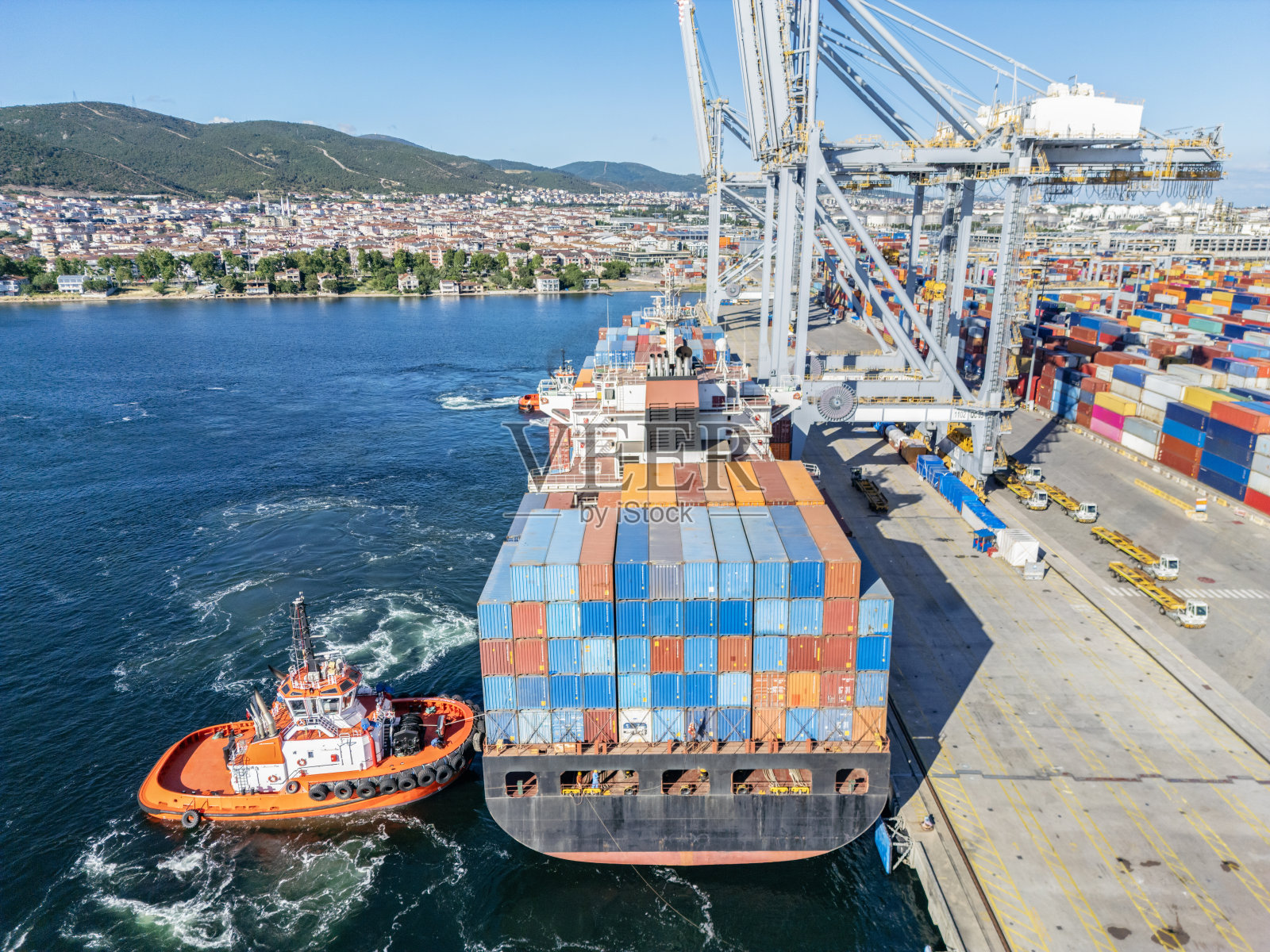 航拍图,集装箱货船正带着拖船驶近港口。照片摄影图片