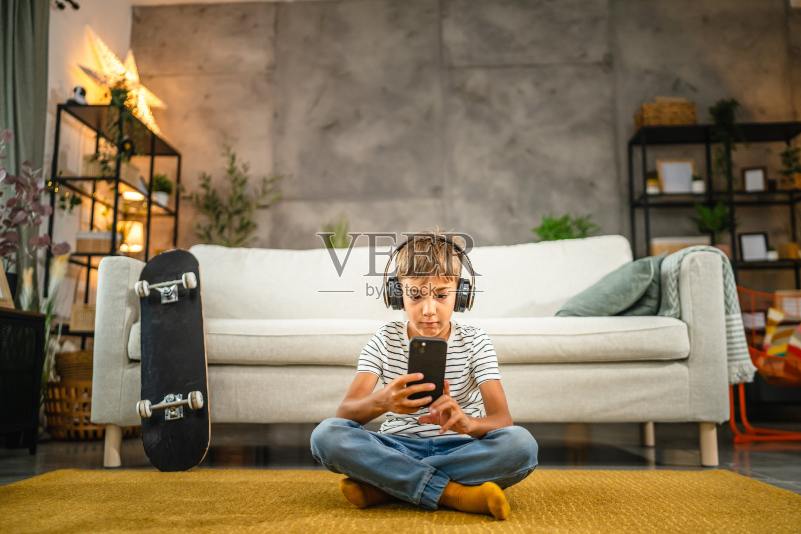 戴着耳机的小男孩坐在地板上玩手机照片摄影图片