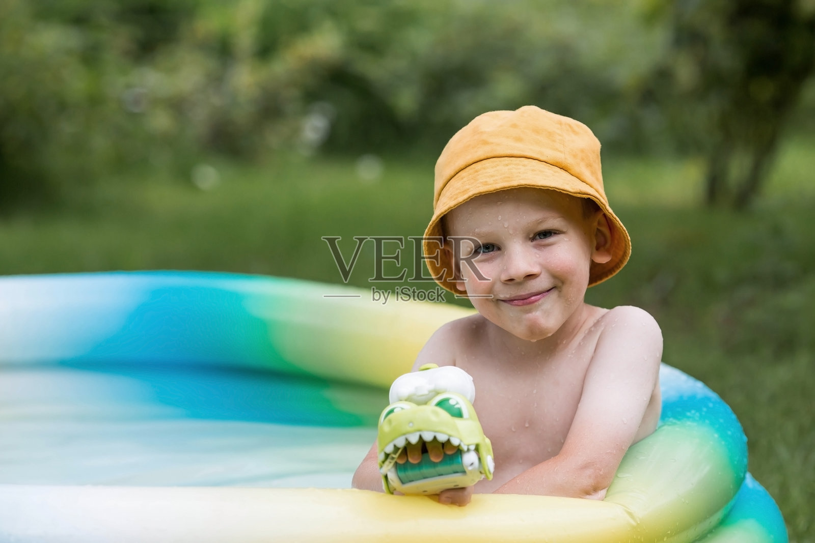 天气很热。一个可爱的男孩正在游泳池里游泳和溅水花。一个快乐的小男孩对着镜头微笑。水花四溅。暑假带孩子的概念。照片摄影图片