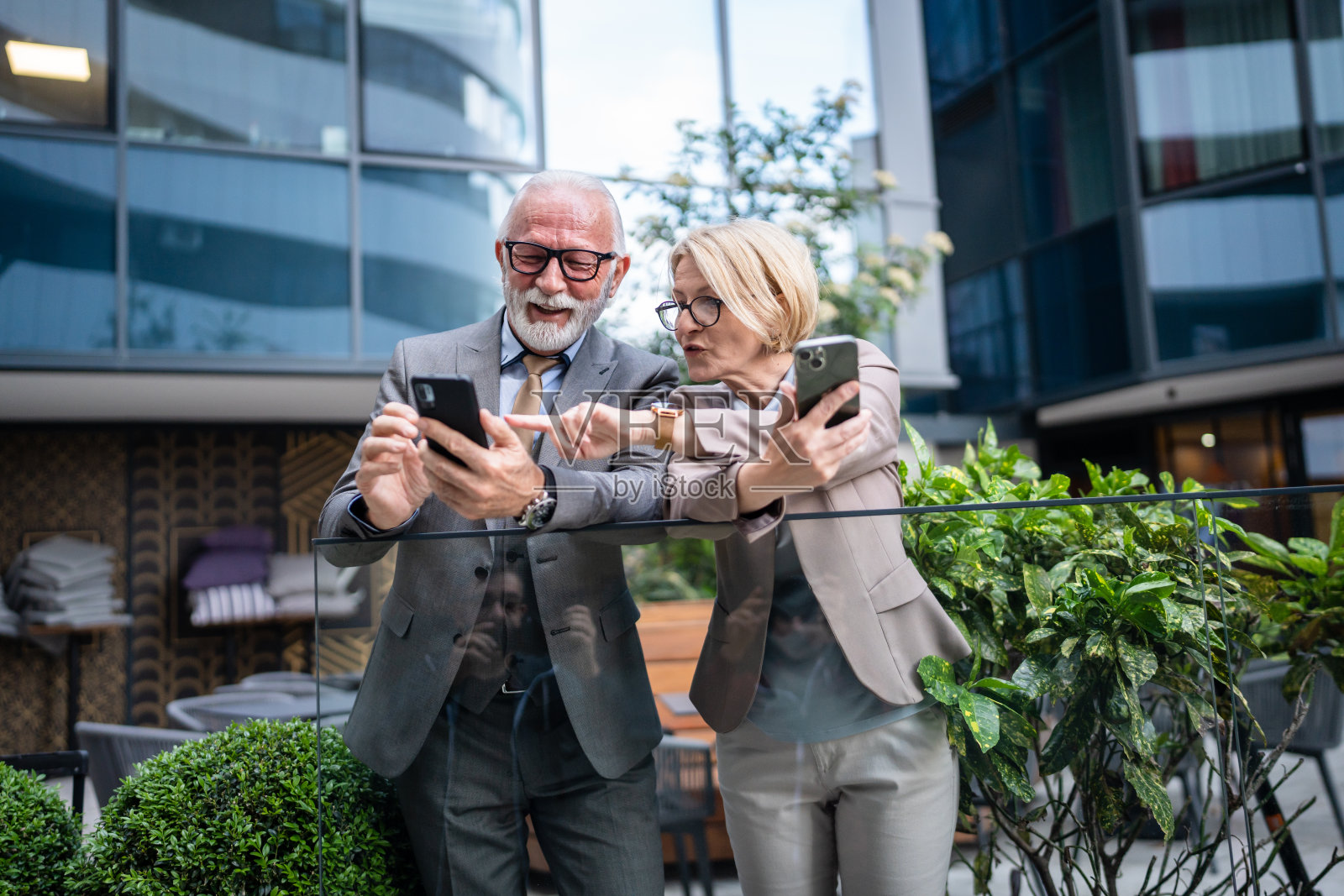 穿着西装的高级男子和成熟的金发女子作为商业伙伴,夫妻朋友或同事聊天,手里拿着智能手机浏览互联网,看照片,交换意见,复制空间照片摄影图片
