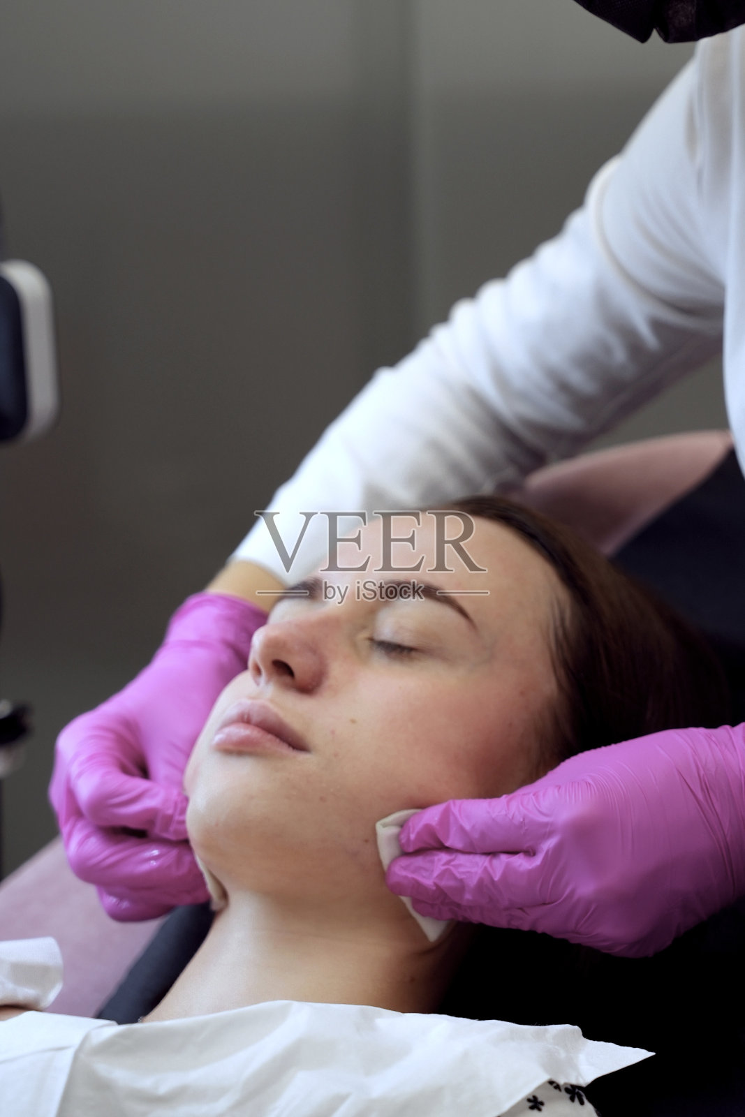 一位戴着粉色手套的美容师正在用海绵擦拭女孩脸上的保湿面膜照片摄影图片