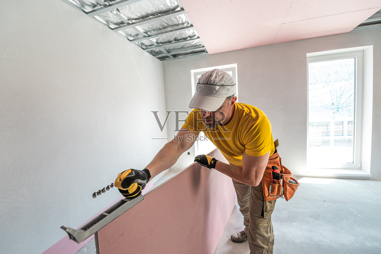 工人做了一个石膏板天花板。他正在用石膏板刨床调整木板的边缘。红色石膏板提高天花板结构的防火性能。照片摄影图片