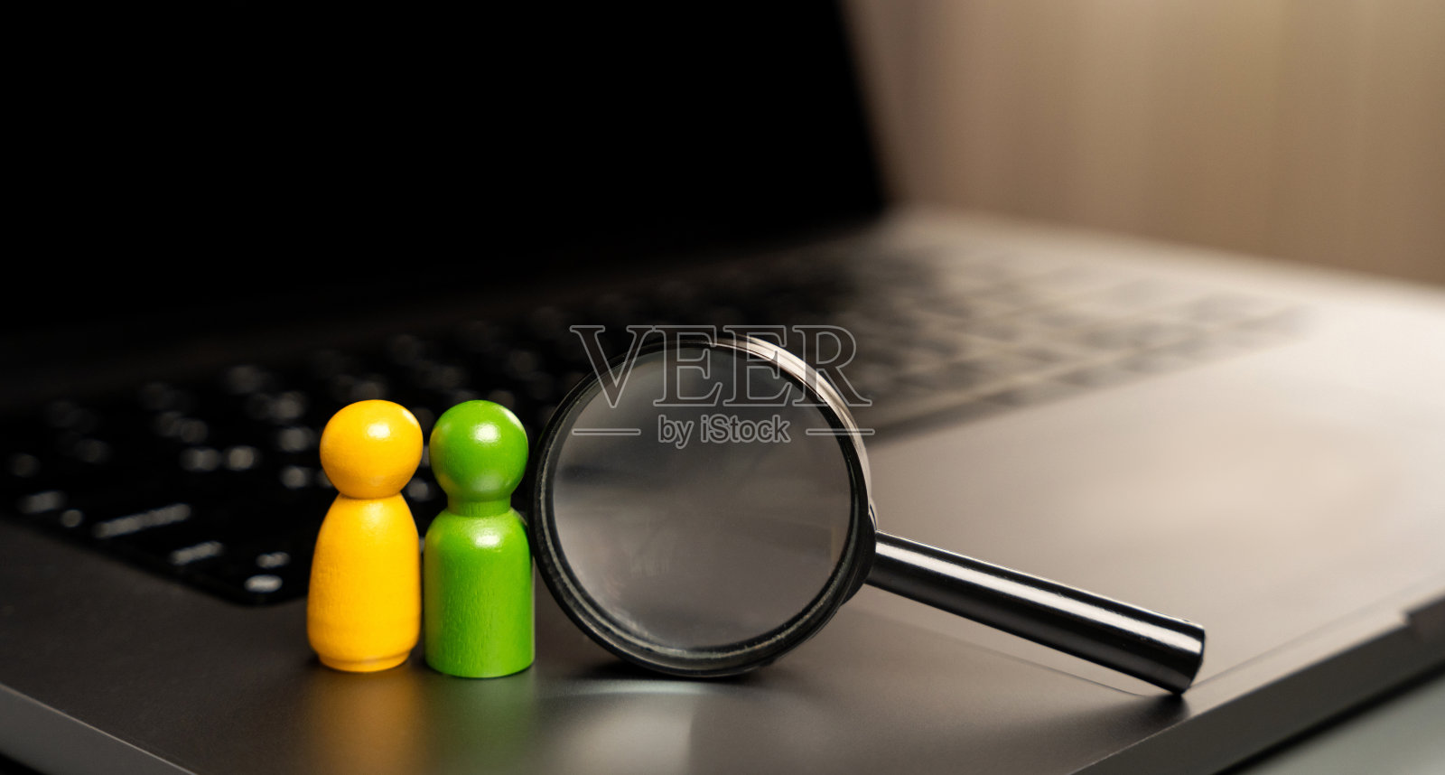 在放大镜旁边的键盘上,立着一对恋人的小雕像。在网上寻找灵魂伴侣和爱情的概念。迷你人物照片摄影图片