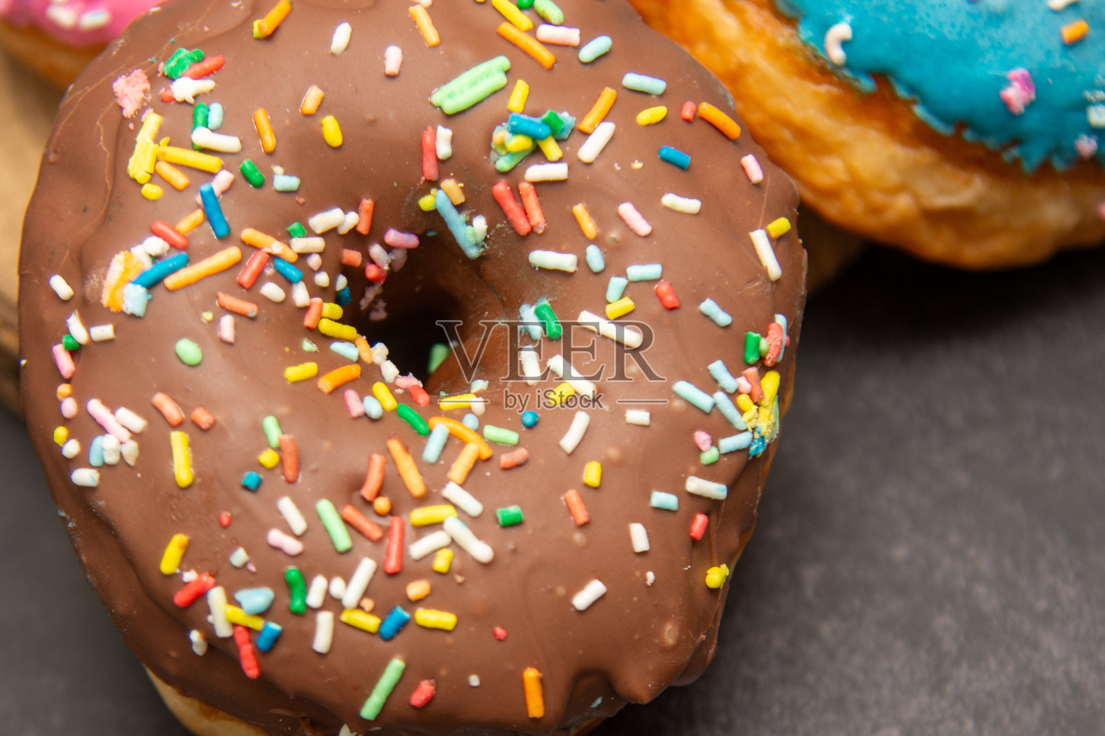美味的甜点。粉色、蓝色和巧克力甜甜圈,上面撒着五颜六色的糖屑。照片摄影图片