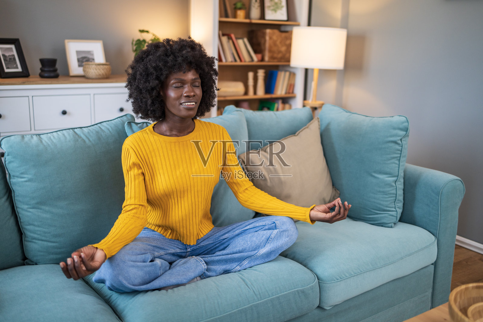 一位非裔美国妇女坐在家里客厅的沙发上练习瑜伽照片摄影图片