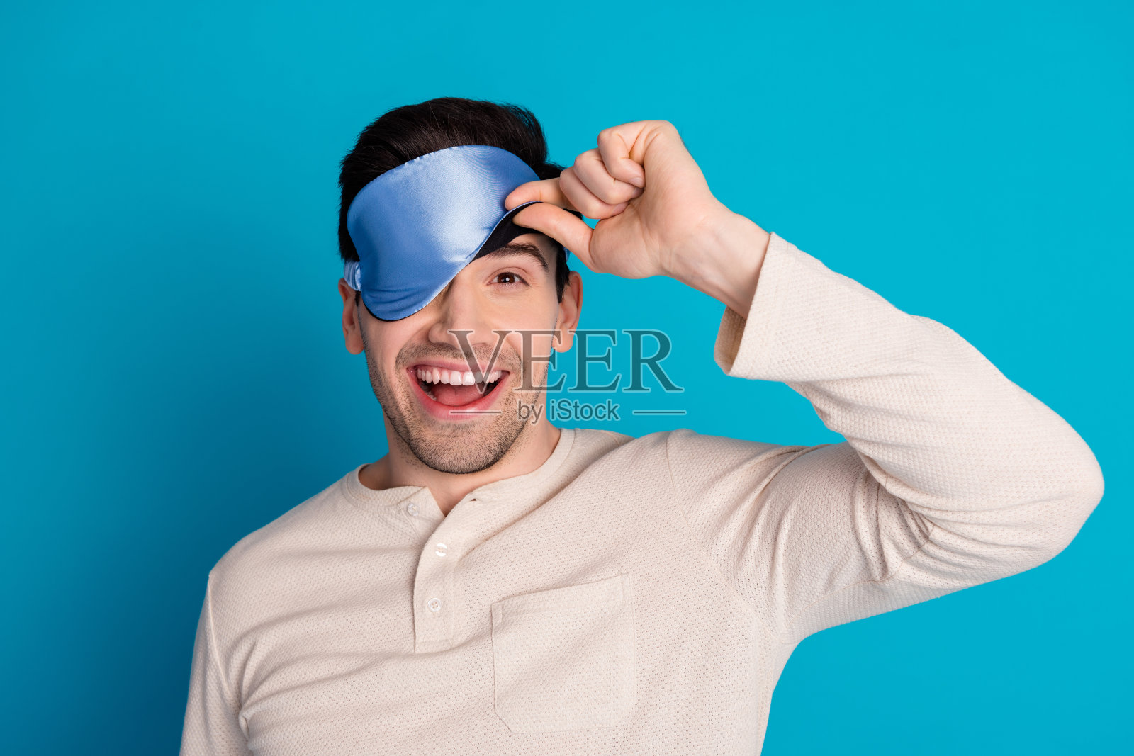 照片肖像英俊的年轻人偷看眼睛蒙着面具睡觉穿着睡衣过夜的人早上好孤立的蓝色背景照片摄影图片