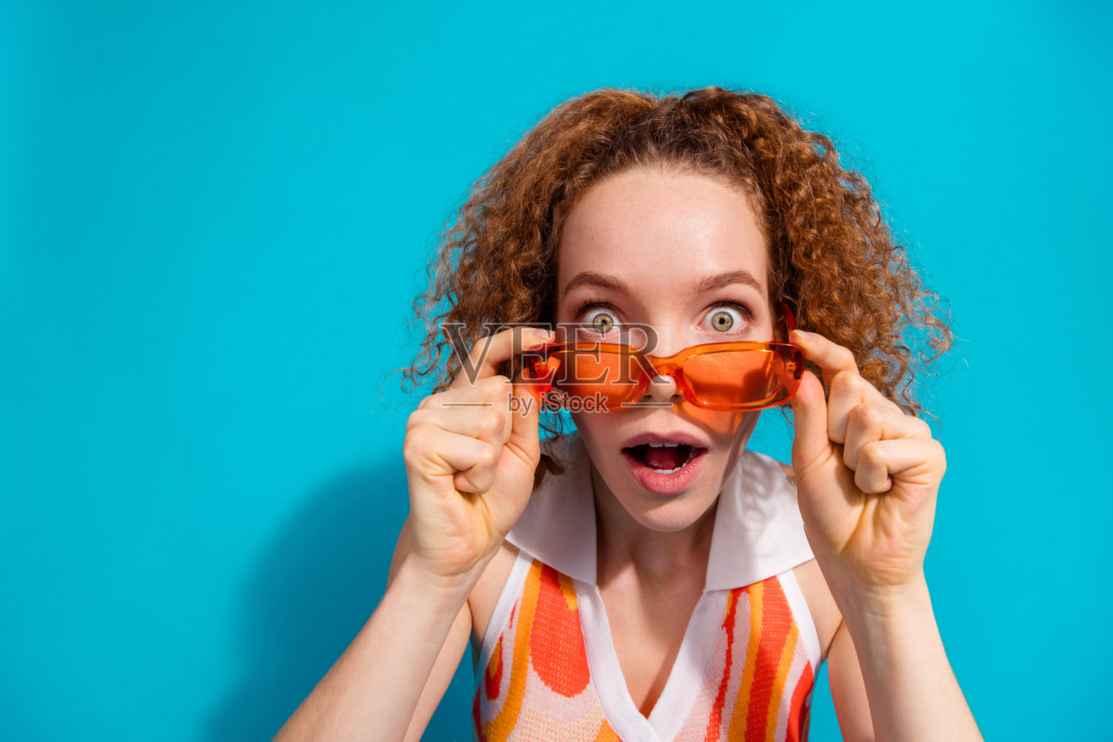 漂亮的年轻女孩的照片肖像,摘下太阳镜,惊讶地穿着时髦的橙色服装孤立的海蓝宝石色背景照片摄影图片