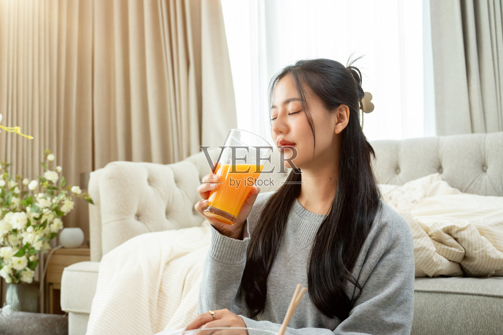 一个迷人的亚洲女人正在客厅的咖啡桌旁喝橙汁。照片摄影图片