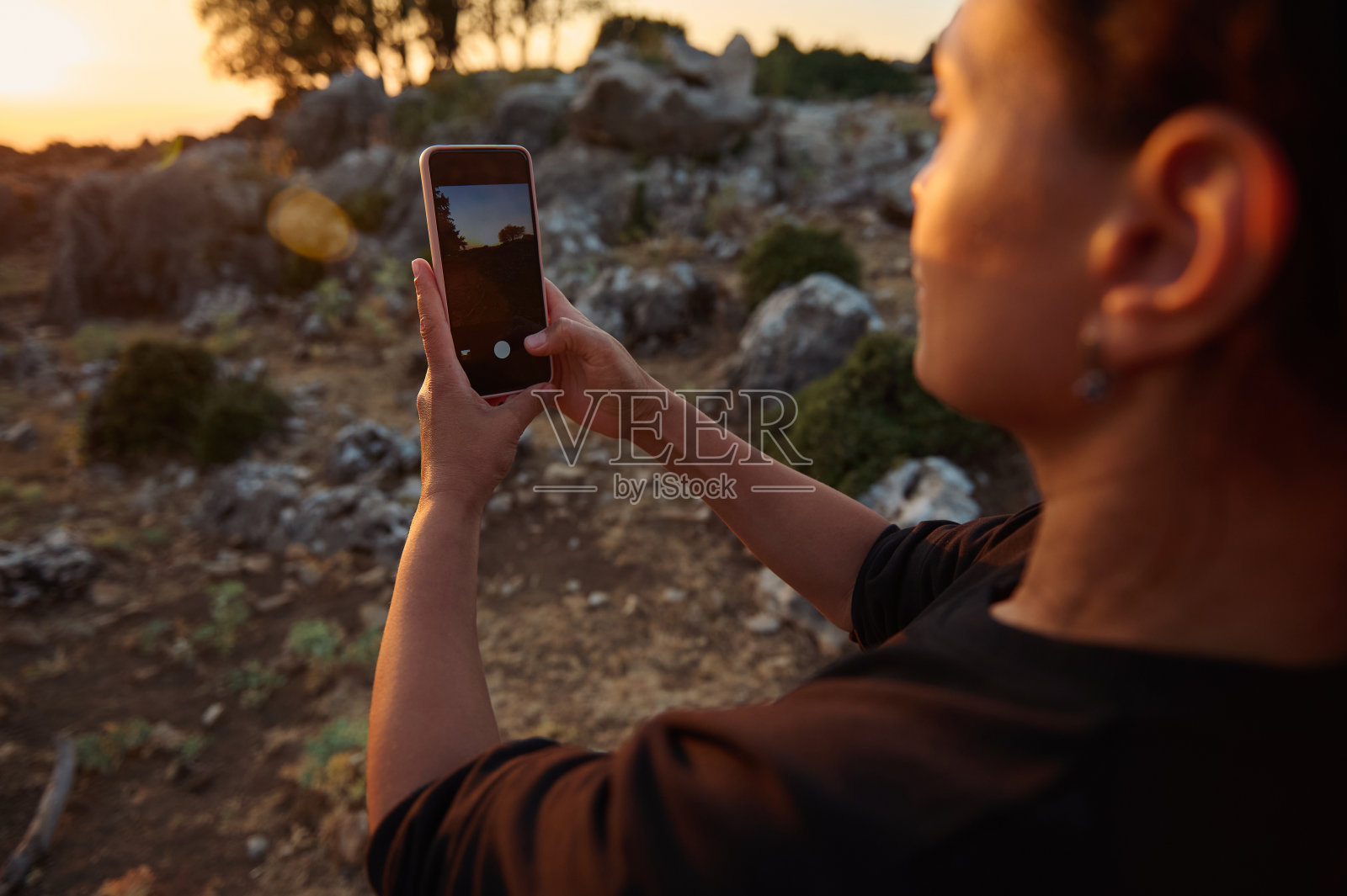 女人在户外岩石地形用智能手机拍摄日落美景照片摄影图片