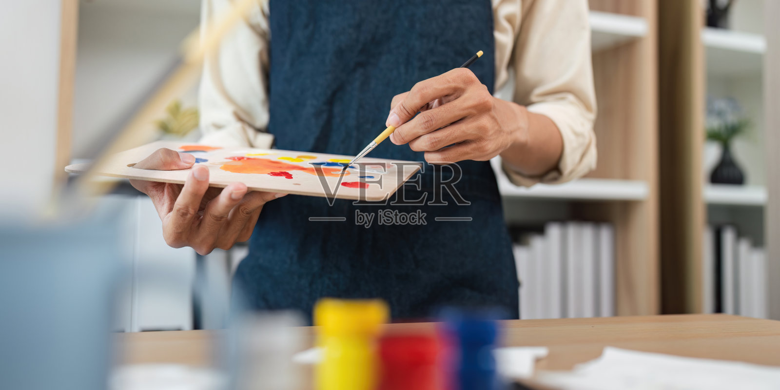 艺术家在工作室用调色板和刷子绘画,创作过程,近距离的手,背景中的艺术用品照片摄影图片