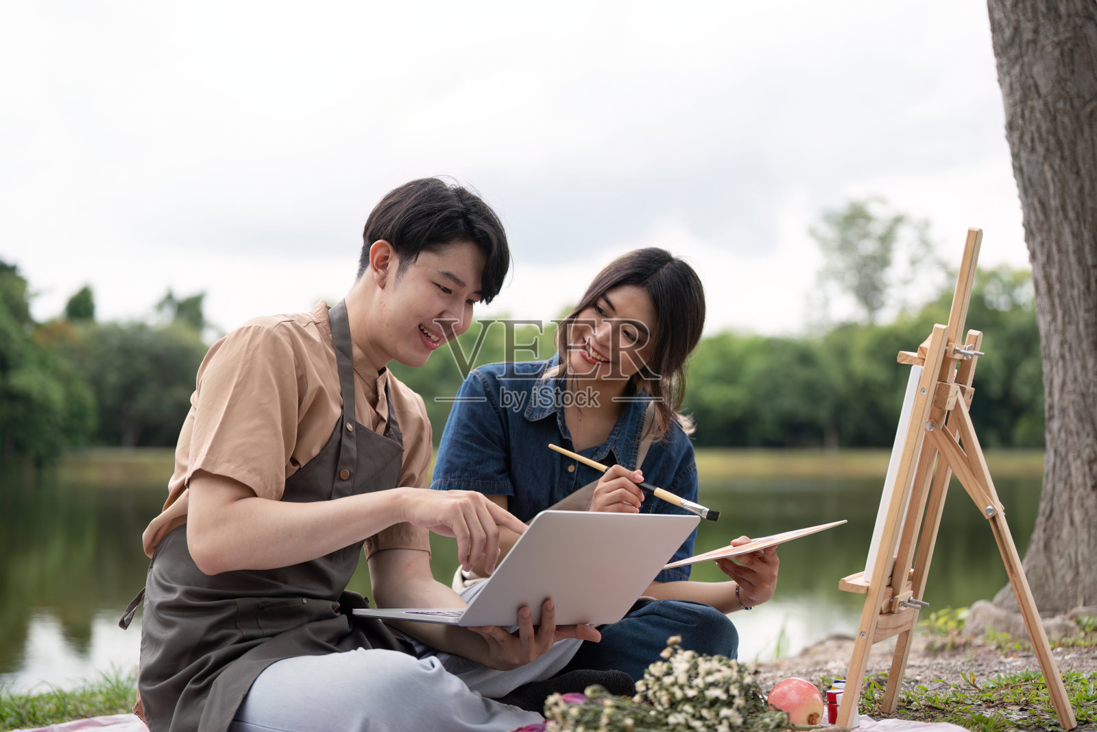 浪漫野餐情侣在湖边画画。与微笑的艺术家一起在大自然中创作艺术照片摄影图片