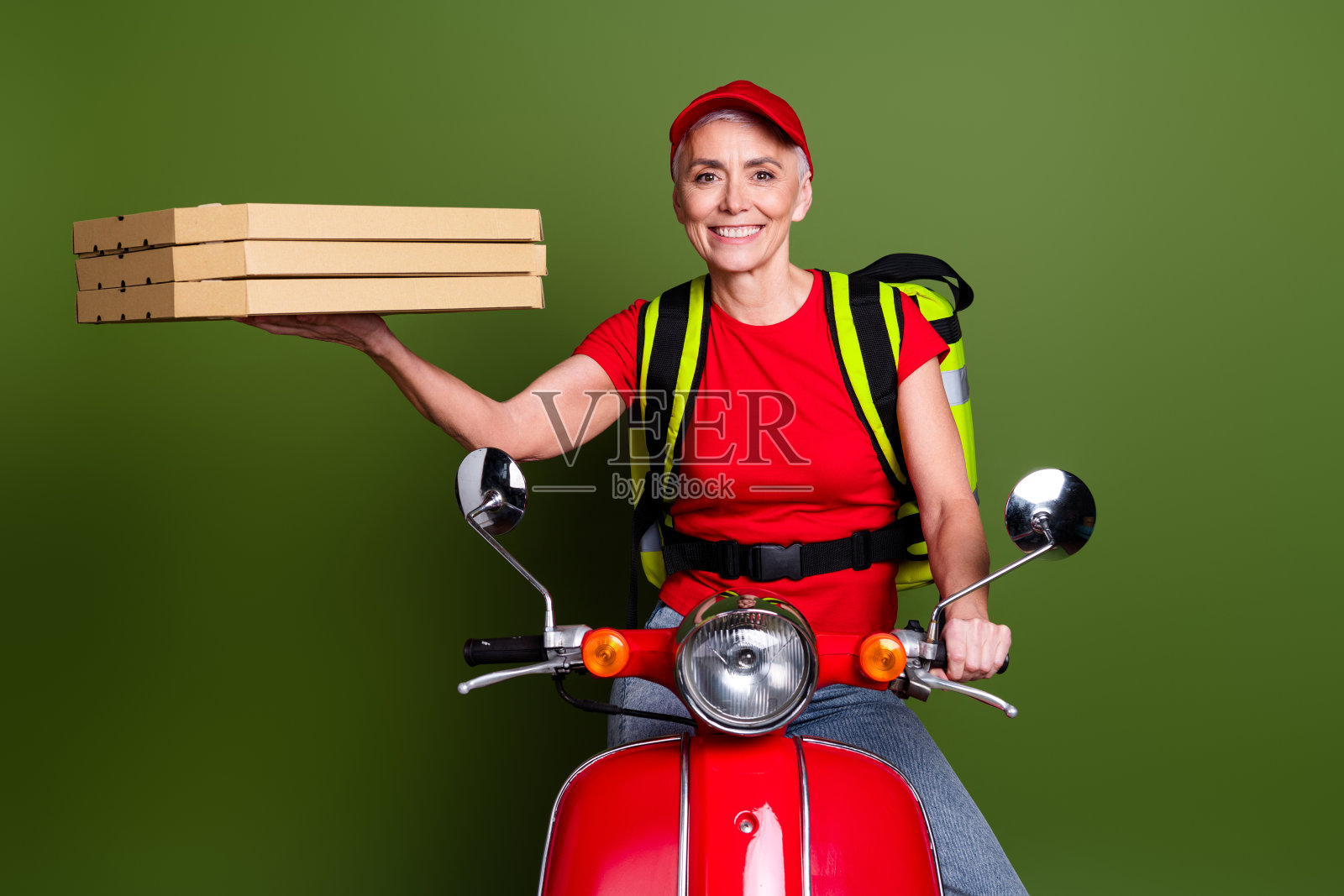 高级女专业外卖员工的照片,保暖袋滑板车披萨,穿着红色制服工作服,隔离在卡其色背景上照片摄影图片