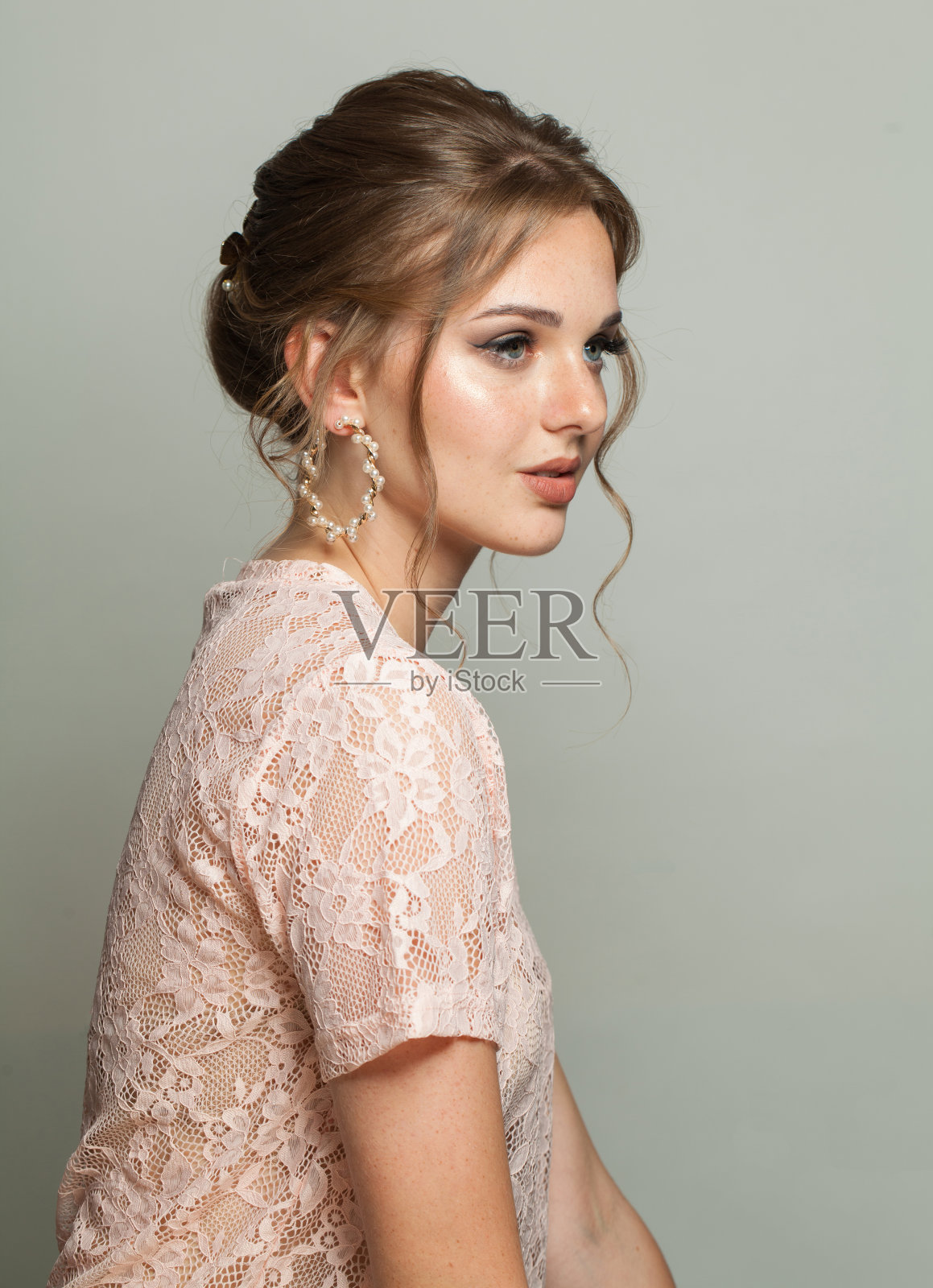 好看迷人的女人时尚模特与化妆和高髻发型在灰色的工作室背景照片摄影图片