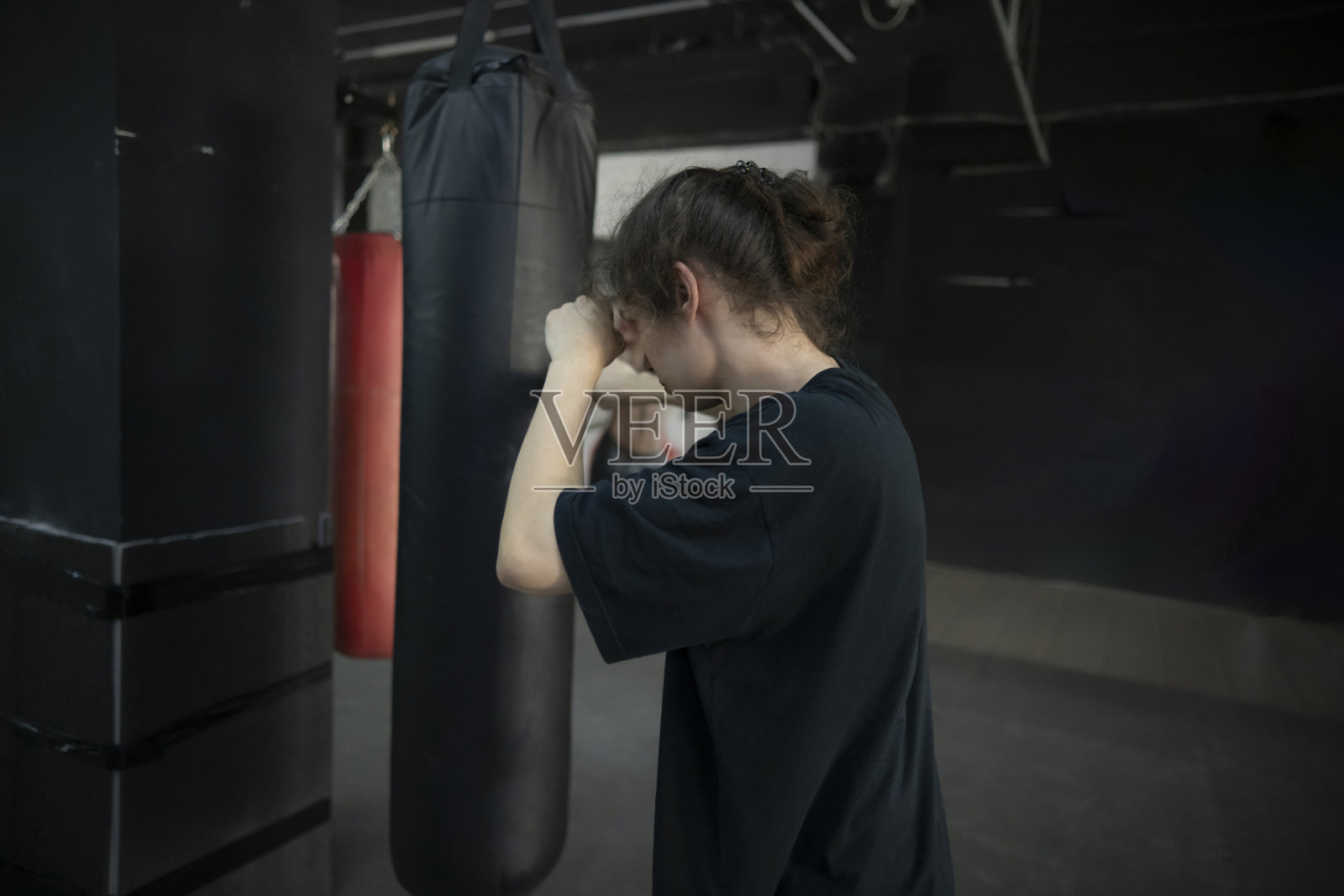 健身房里,一个穿着黑色t恤的男人在打一个黑色的沙袋。这个男人很专注,很有决心照片摄影图片