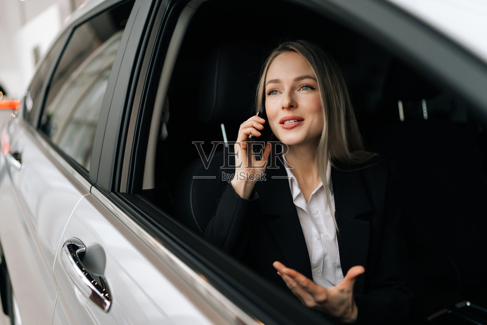 女商人坐在车里用智能手机聊天,聊得很愉快。开朗的金发女老板和工人们通电话照片摄影图片