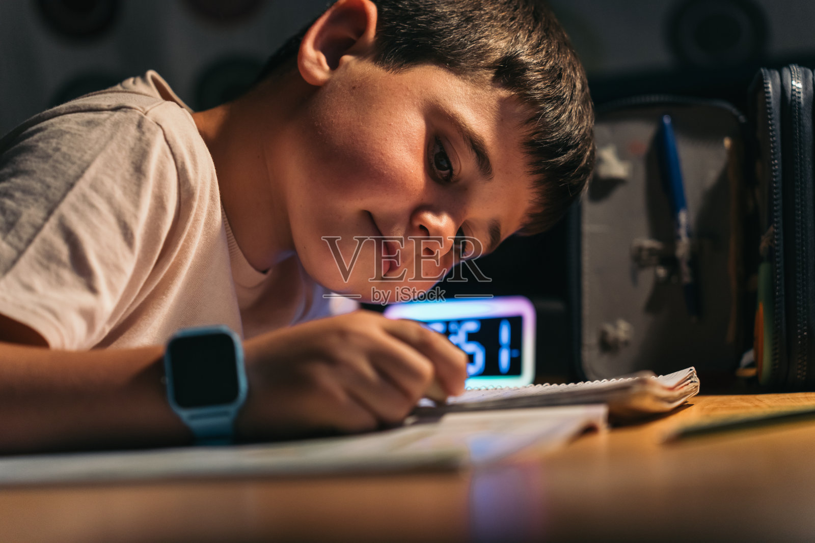 专注的年轻学生在晚上擦作业。年轻的学生晚上坐在书桌前专心做作业照片摄影图片