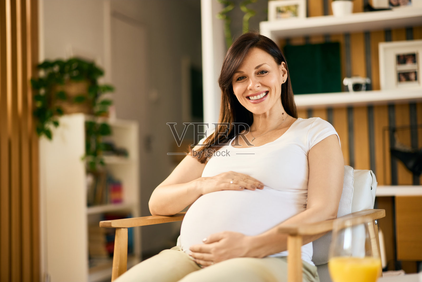 一个可爱的孕妇的肖像,抱着肚子,对着镜头微笑。照片摄影图片