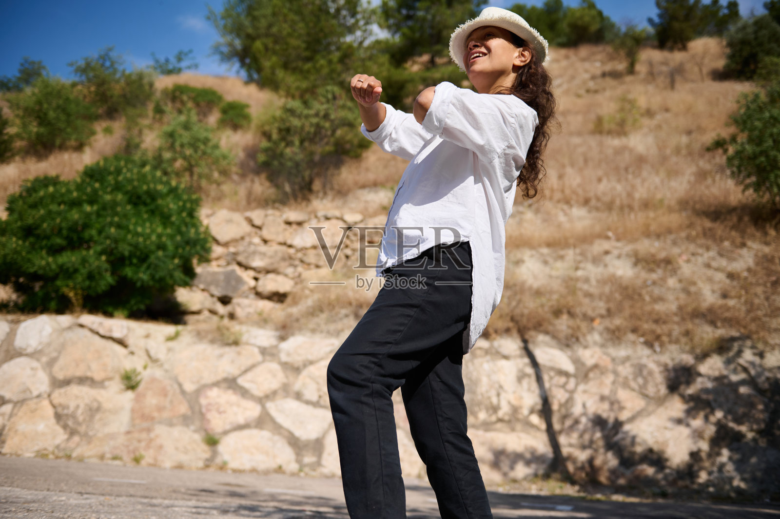 在大自然中跳舞的女人,享受着阳光明媚的一天,穿着白色的衬衫和帽子照片摄影图片
