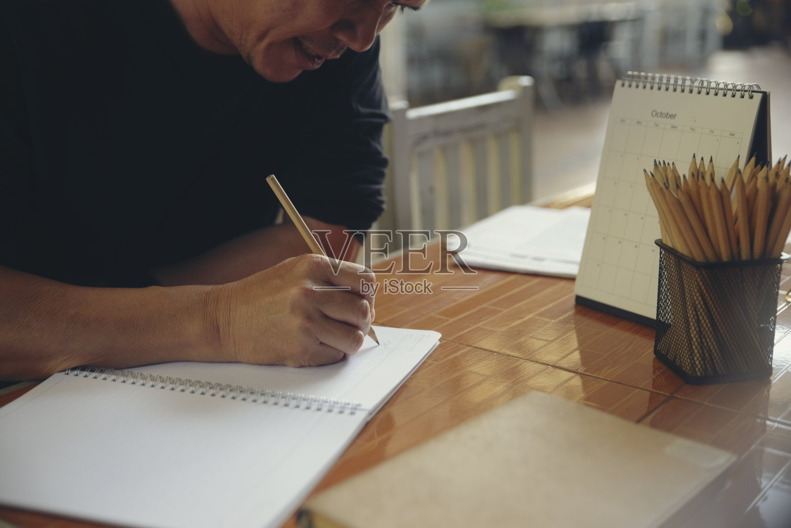 男计划员的手写每天的约会日历簿,工作空间在家里。在办公桌旁使用智能手机,在日记本上计划并记录日程安排(假期旅行)。计划的概念。照片摄影图片