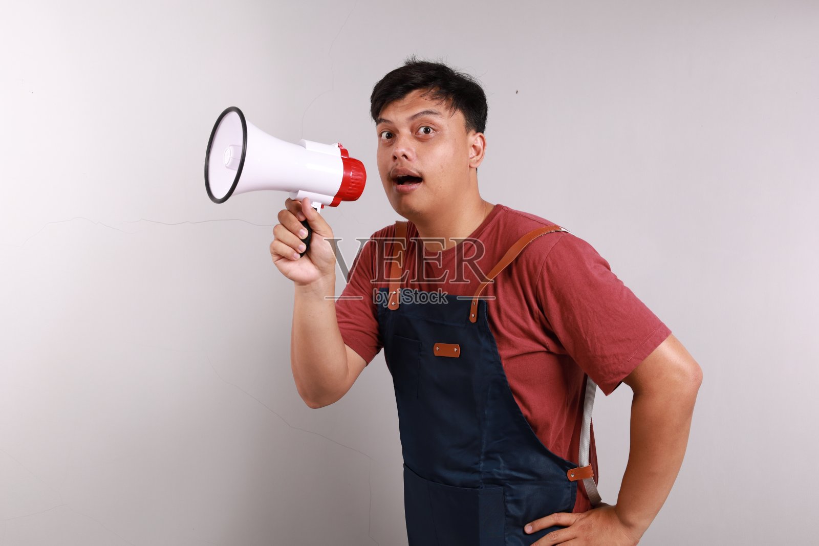 年轻的亚洲男子,咖啡师,酒吧服务员,穿着蓝色围裙,站在咖啡店工作,手里拿着扩音器照片摄影图片