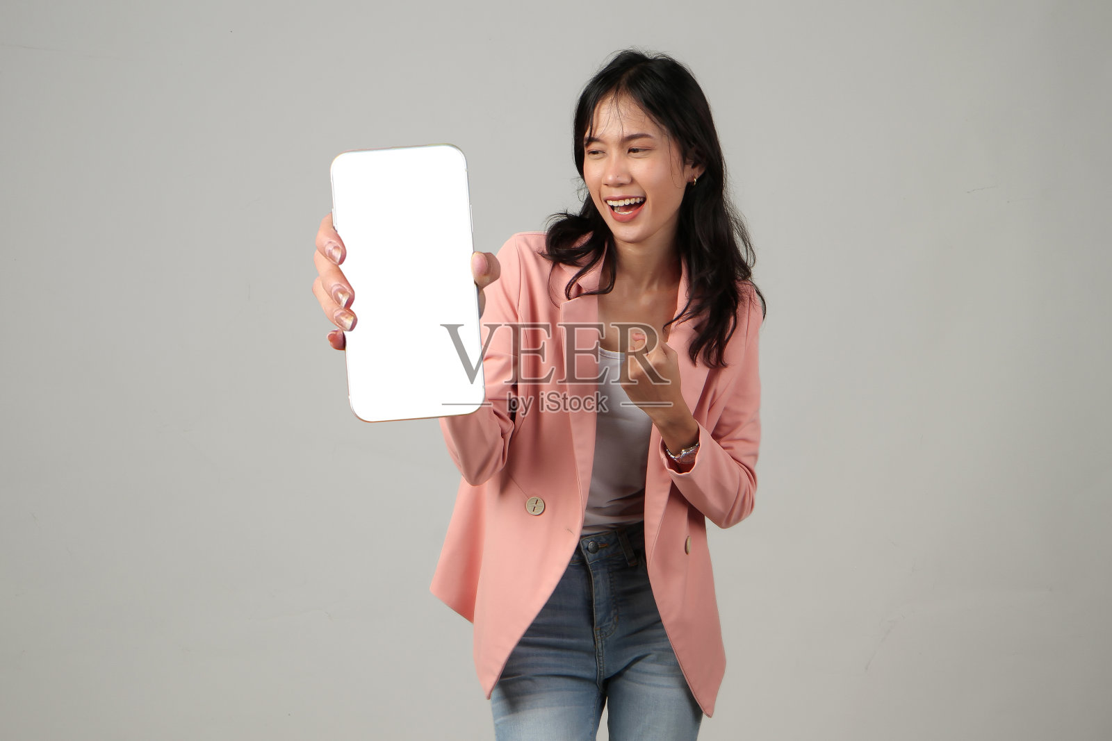 快乐的亚洲女人在孤立的背景下用拇指向上的手势展示手机空白屏幕照片摄影图片