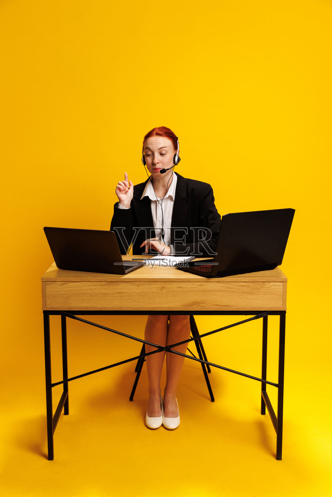 呼叫中心员工,穿着正式服装的女性,正在打电话,桌子上有两台笔记本电脑,背景是黄色的照片摄影图片