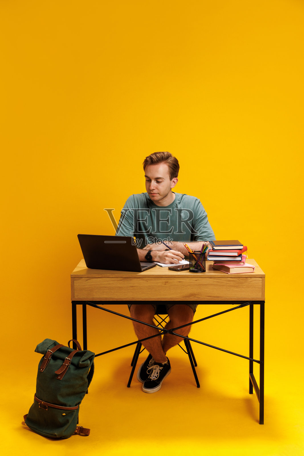 小男孩,学生坐在课桌前,参与深度学习,用笔记本电脑听在线课程,在黄色背景下做笔记照片摄影图片