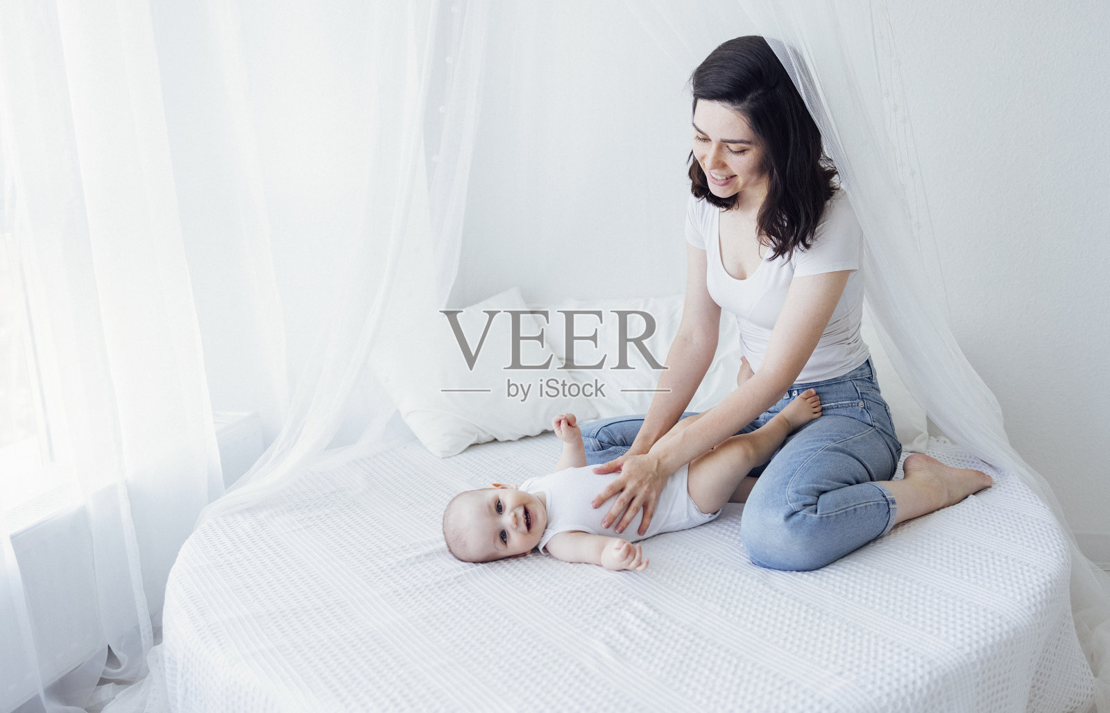 穿着白色紧身衣的漂亮婴儿和浅色背景下的妈妈。母亲的概念。照片摄影图片