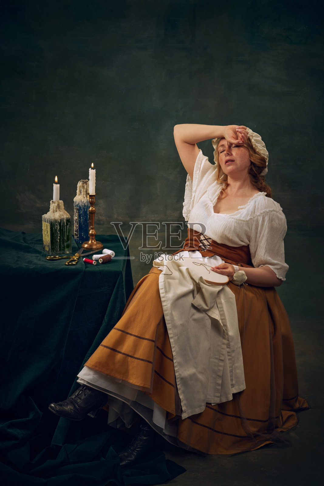 年轻女子穿着古着缝制的衣服,坐在桌旁感到疲惫,背景是古着的绿色。照片摄影图片