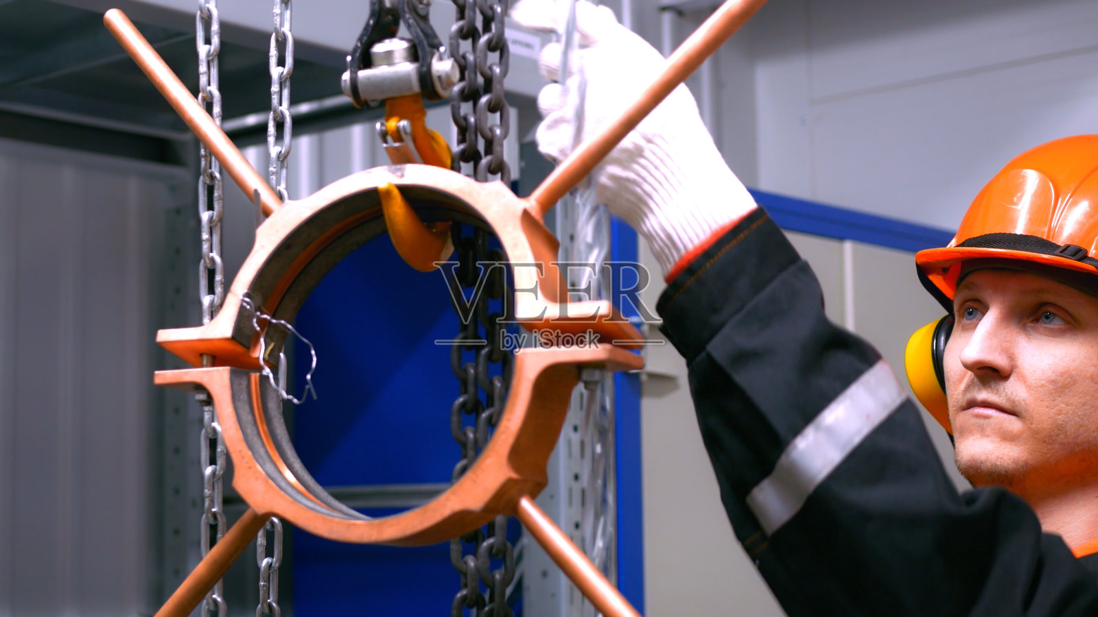 工人戴着安全装置操作起重机械,以处理金属物体。设备包括手套、头盔和其他工业环境必需的防护装备。垂直视频照片摄影图片