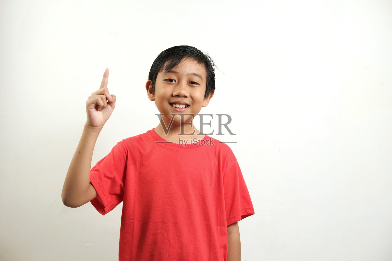 一个穿着红衬衫的男孩微笑着用食指指着白色背景。照片摄影图片