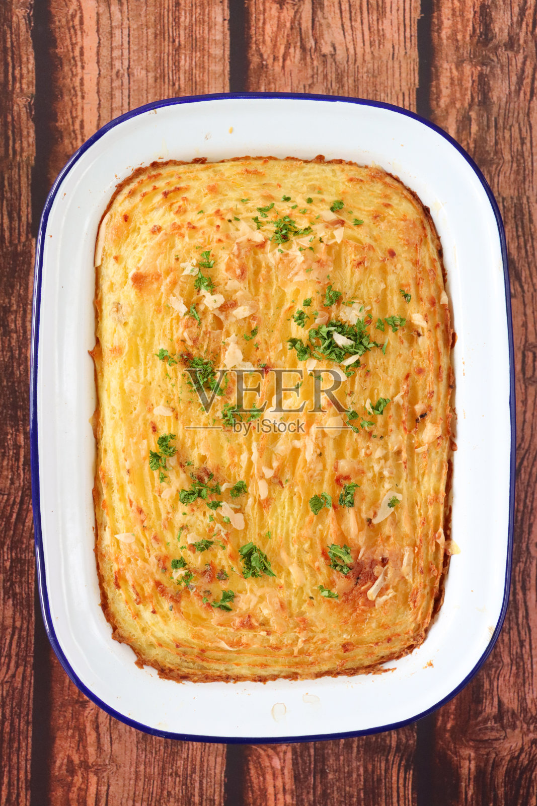 熟的,自制的鱼馅饼,鲑鱼,鳕鱼和烟熏黑线鳕块,磨碎的胡萝卜,韭菜,红辣椒在珐釉质烤箱盘,脆金黄,土豆泥配上叉形图案,木纹背景,高架视图照片摄影图片