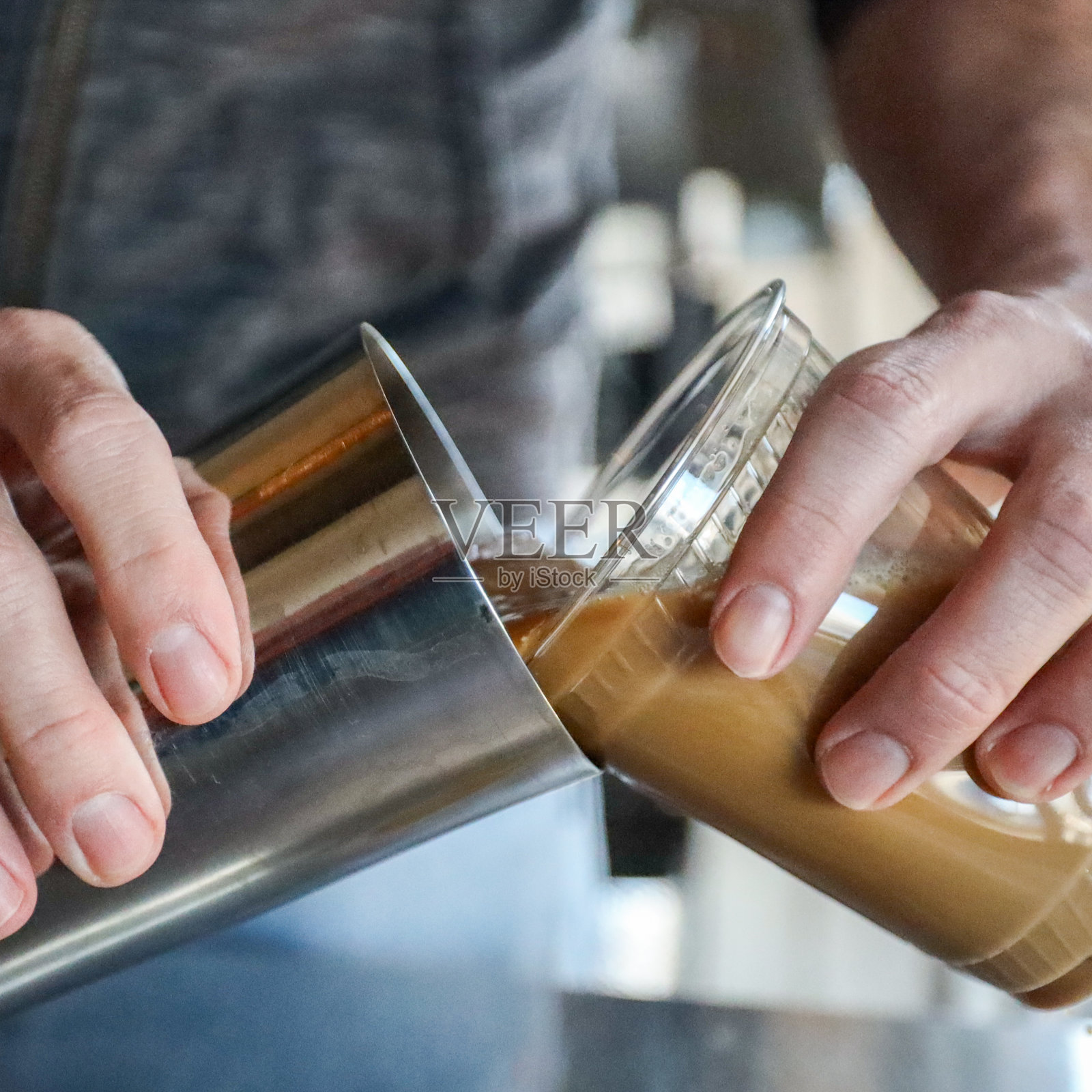 男咖啡师的手从摇壶中倒入棕色奶油咖啡冷萃到透明塑料杯的特写照片摄影图片