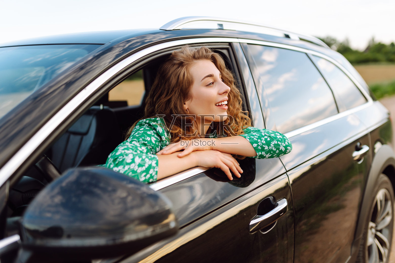 美丽的卷发女人享受大自然,看着窗外的汽车。照片摄影图片