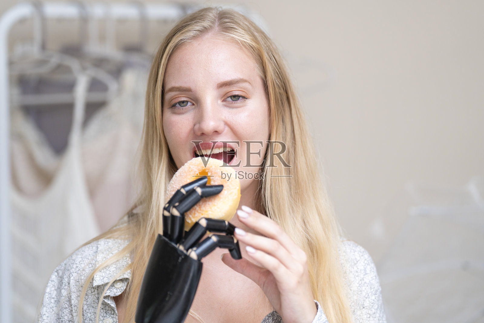 一名年轻女子正在使用附着在她身体上的机械假肢。她控制她的手拿起物体食物甜甜圈。这位女士试图控制家中的智能手臂。照片摄影图片