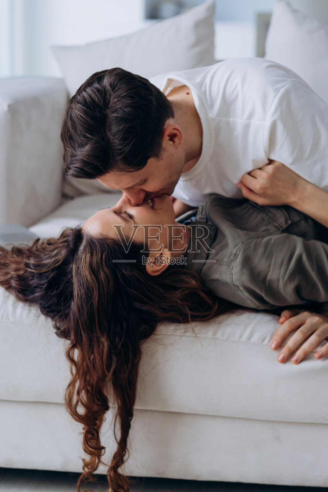 一个男人温柔地亲吻他的伴侣,捕捉他们在沙发上放松时的温柔和爱的时刻。他们的亲密描绘了一种深厚的联系和感情。照片摄影图片