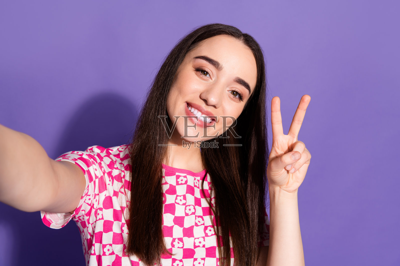 一名漂亮的年轻女子自拍,v字标志,身穿紫色背景的格子t恤照片摄影图片