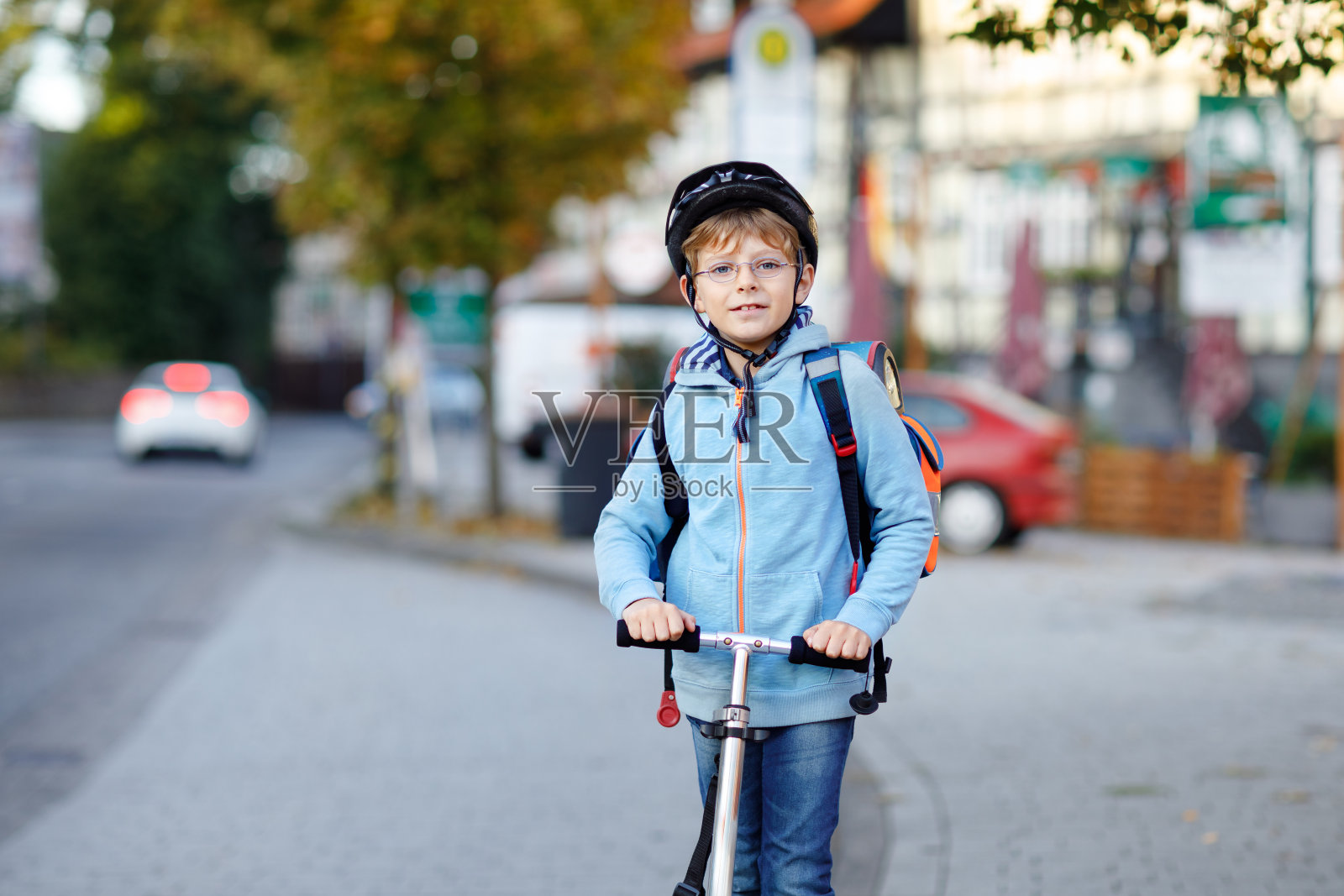 阳光明媚的日子里,活跃的小学生戴着安全帽,背着背包在城市里骑着他的摩托车。快乐的孩子穿着五颜六色的衣服骑自行车上学。照片摄影图片