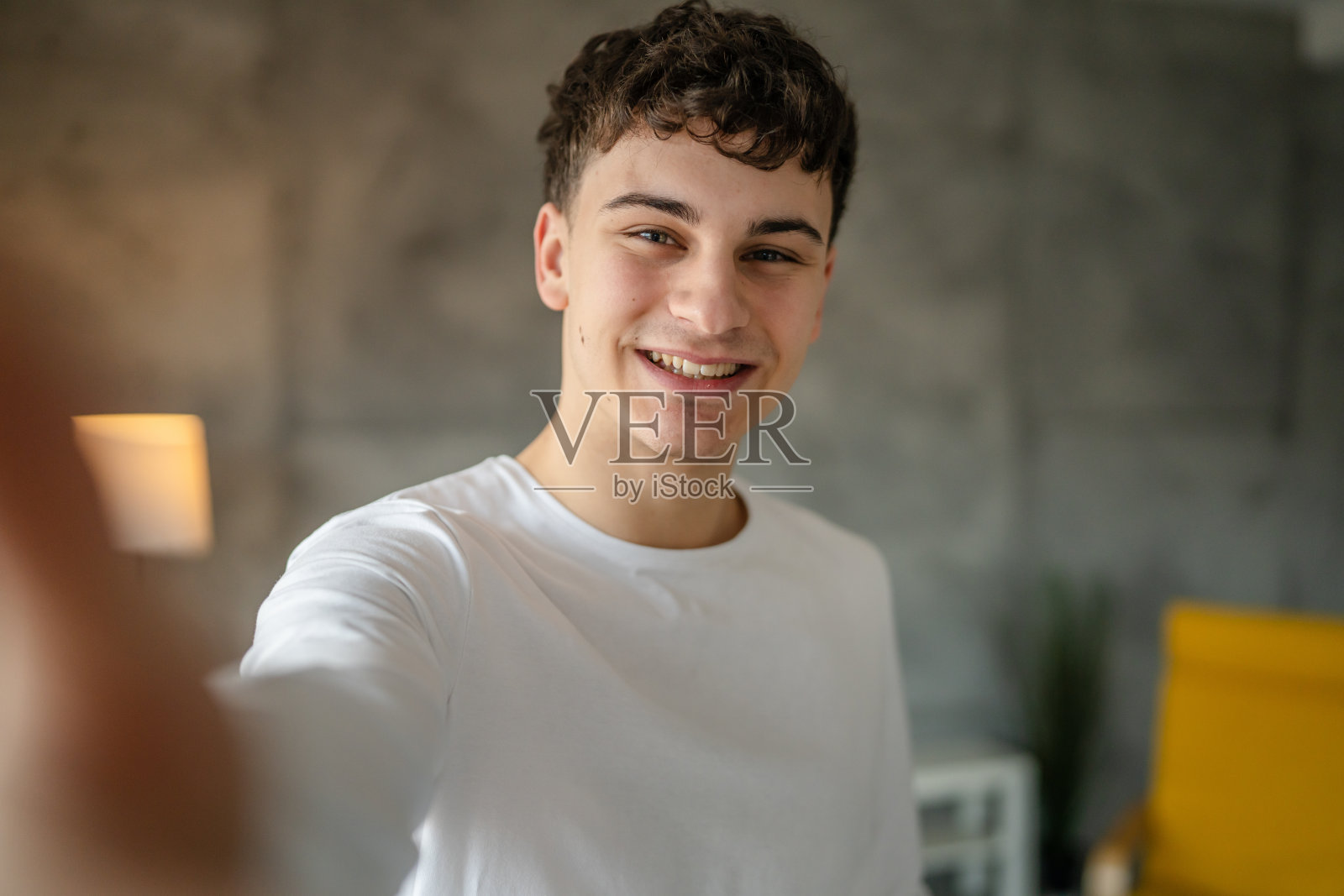 一名20岁的白人男子在家里微笑着看着镜头,穿着休闲的白衬衫照片摄影图片