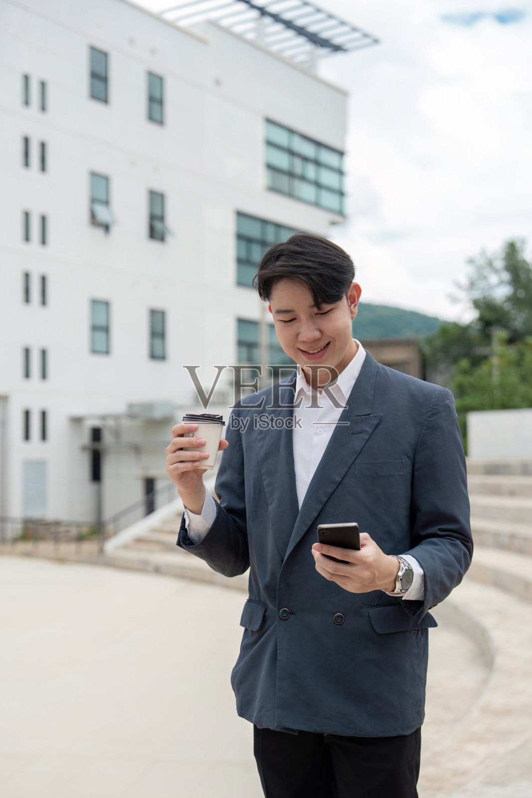 年轻的商人在现代办公大楼外一边喝咖啡一边查看智能手机照片摄影图片