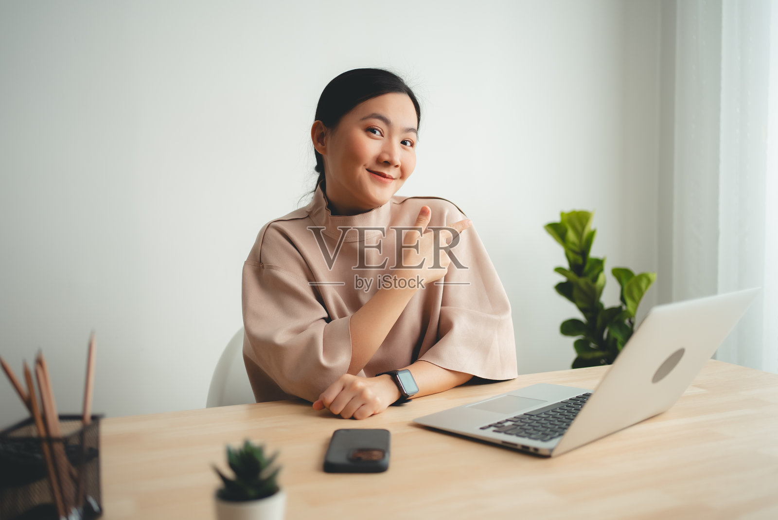 亚洲妇女开心地微笑着展示复印空间,坐在家里的办公室里看着镜头。照片摄影图片