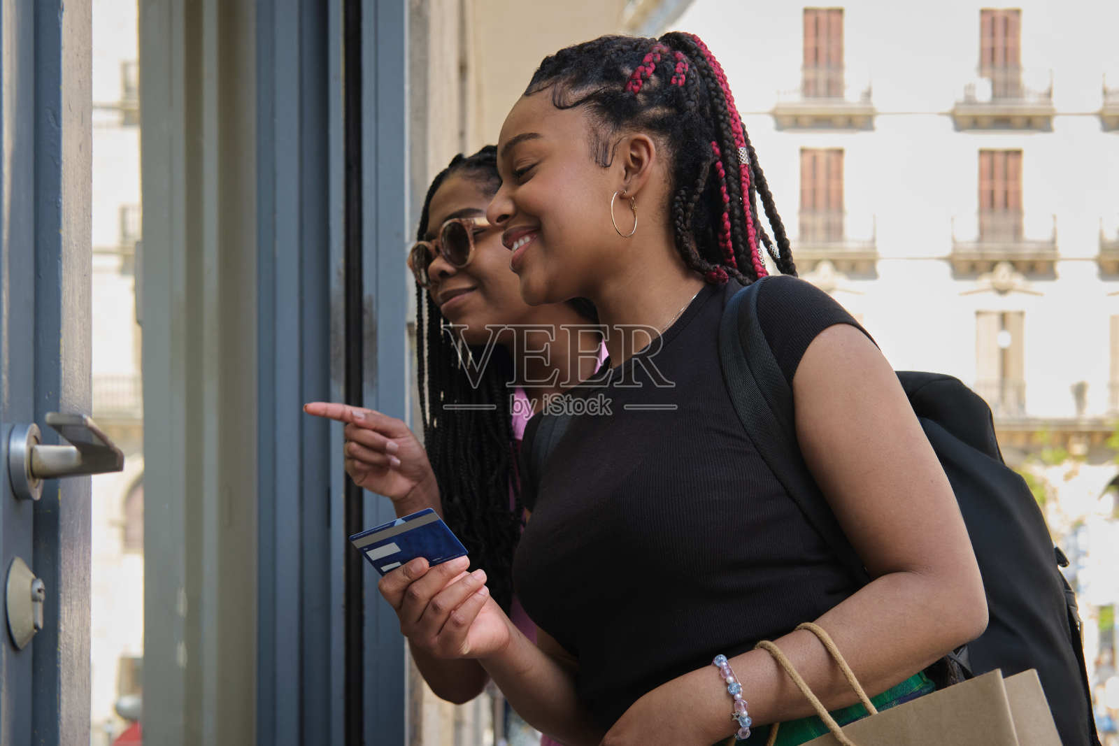 两个朋友的侧视图肖像美丽和自信的拉丁裔年轻女性与一个漂亮的发型看着商店的橱窗和交谈拿着信用卡在户外购物照片摄影图片