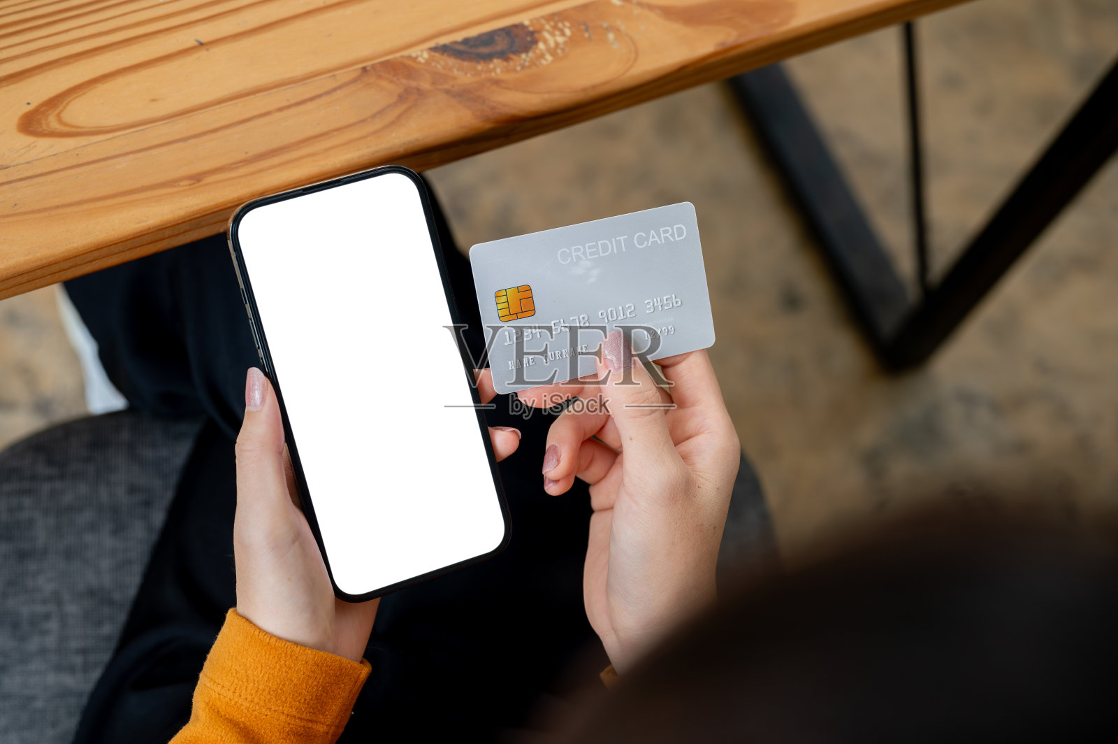 一张特写俯视图,一位女士坐在桌子旁,手里拿着信用卡和智能手机。照片摄影图片