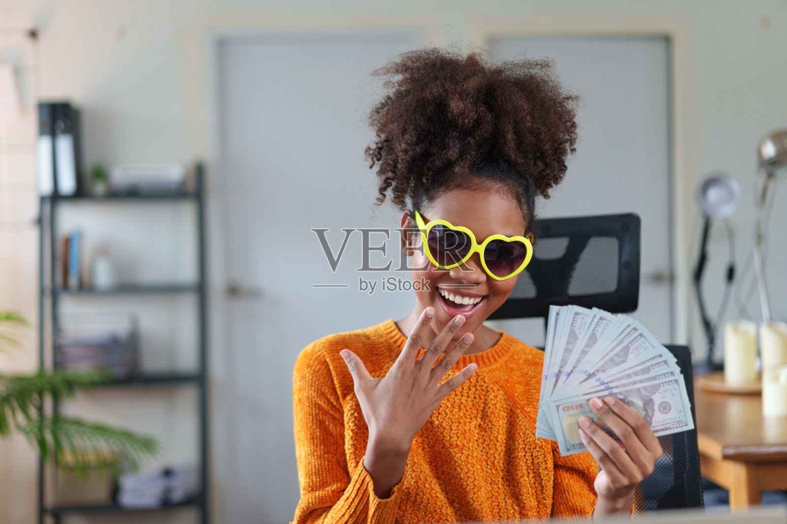 一位年轻的非裔美国妇女,脸上带着惊讶的表情,手里拿着一叠百元大钞照片摄影图片