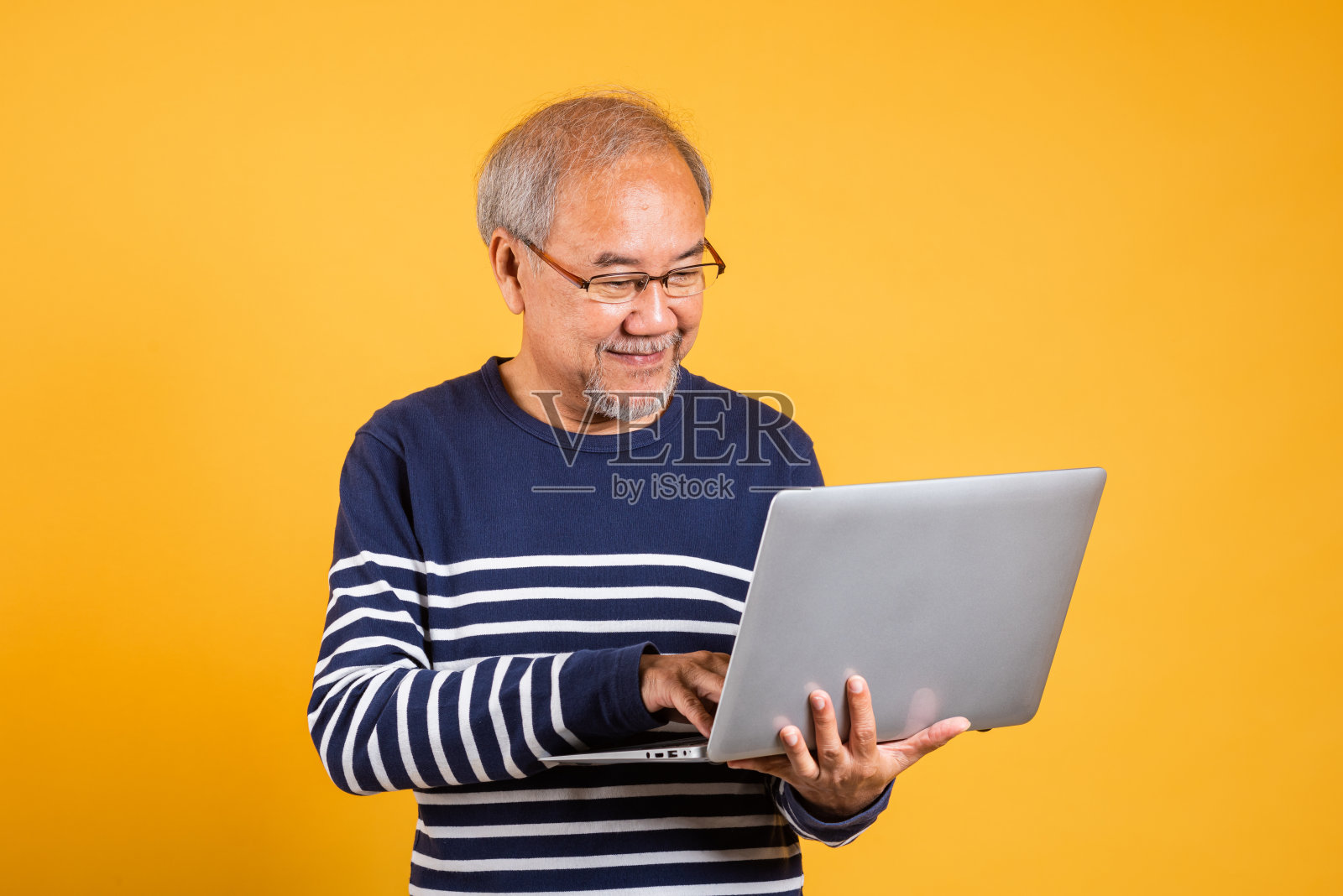 画像上的亚洲老人戴着眼镜,用笔记本电脑工作室拍摄孤立的黄色背景,白发苍苍的老人微笑着快乐地工作照片摄影图片