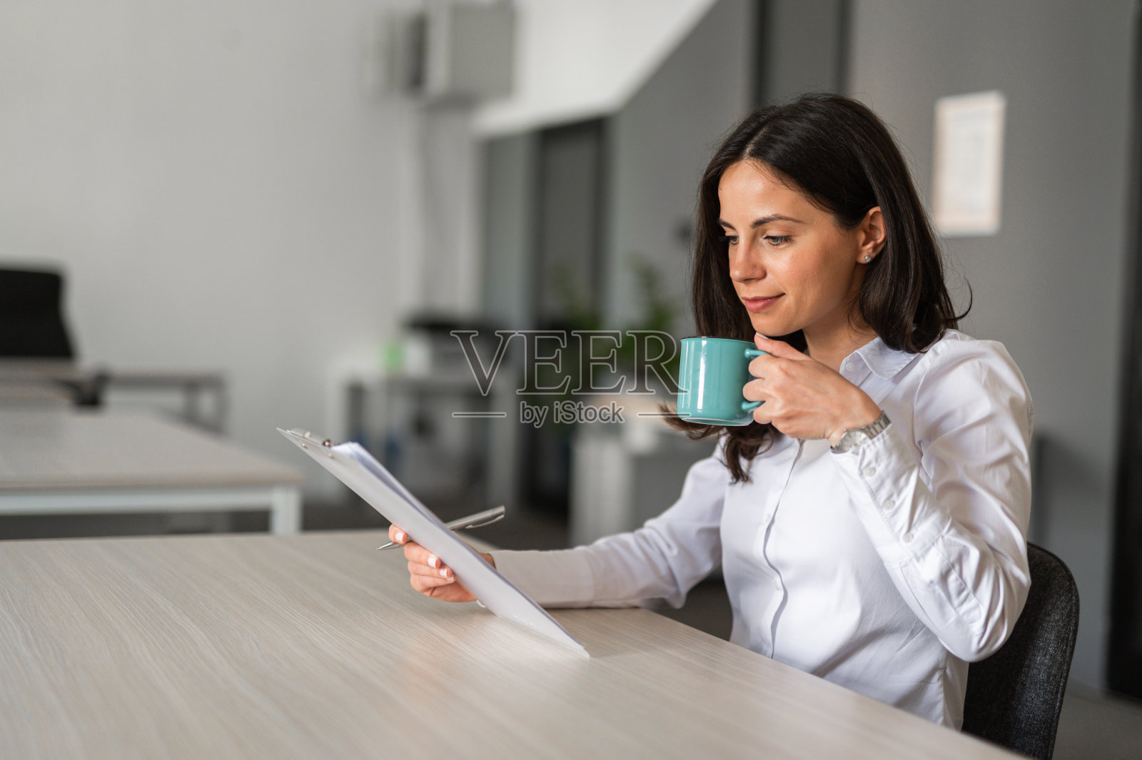 年轻的女企业家,手里端着一杯咖啡,专心地坐在办公桌前阅读文件照片摄影图片